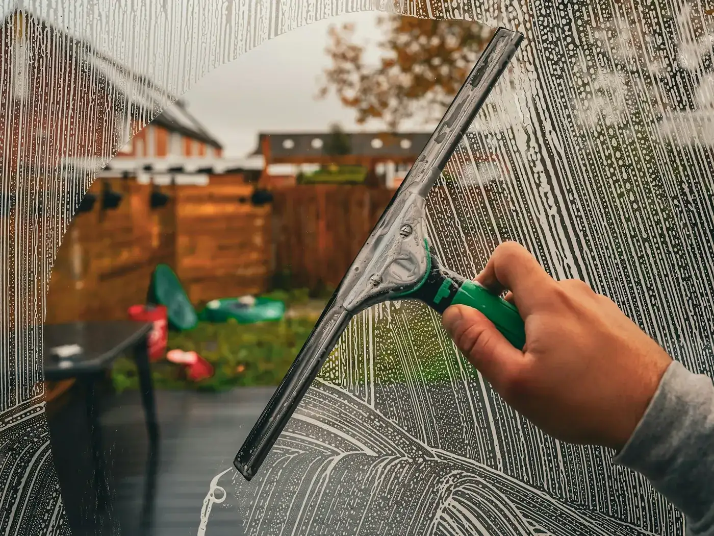 A hand drawing a squeegee across a soapy window pane